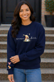 A woman wearing a navy blue sweatshirt with a Winnie the Pooh design and the text "mama bear" printed on it, smiling at the camera.