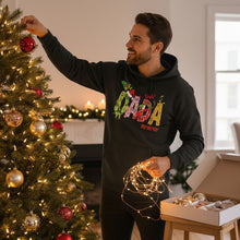 A man in a black hoodie decorating a Christmas tree with ornaments and lights.
