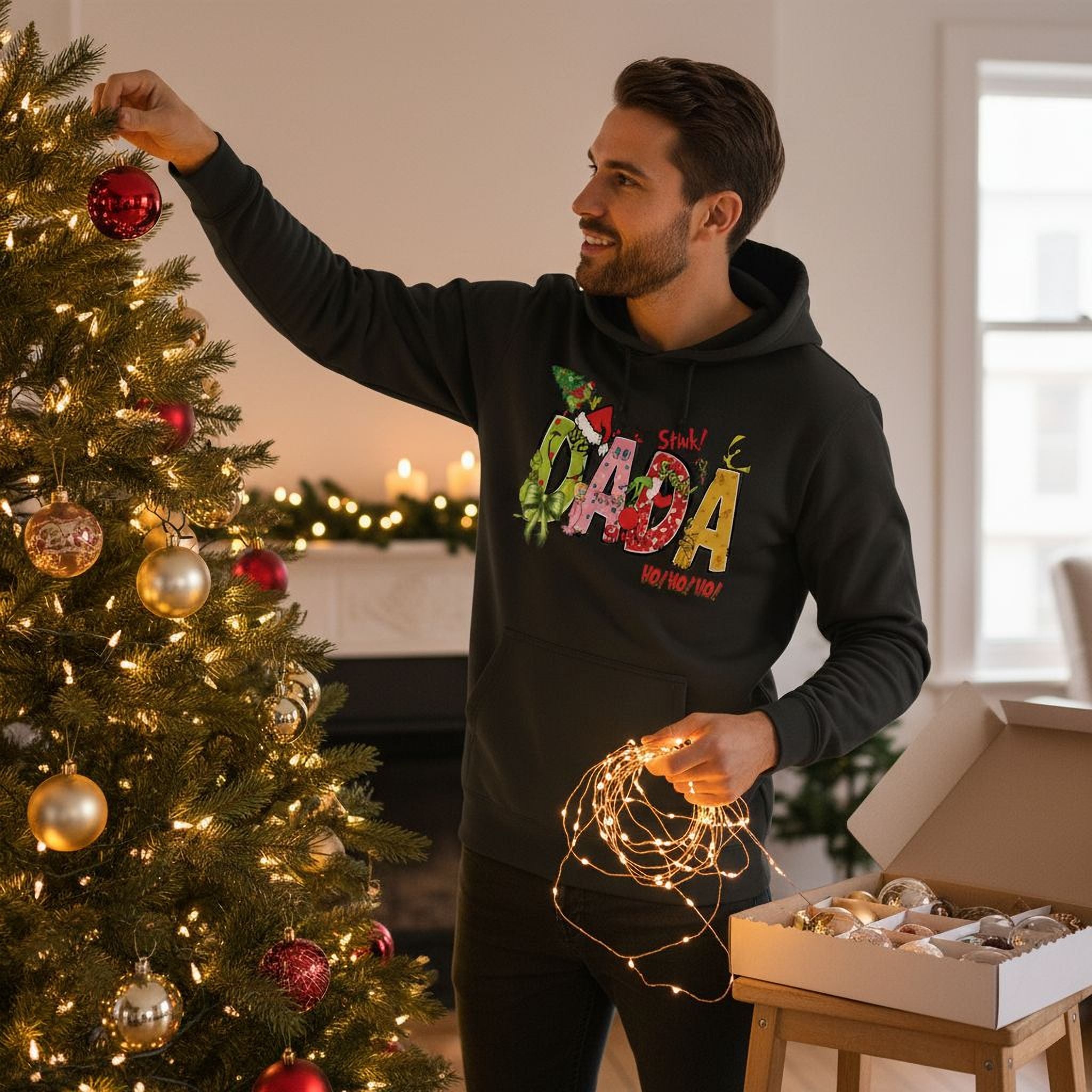A man in a black hoodie decorating a Christmas tree with ornaments and lights.