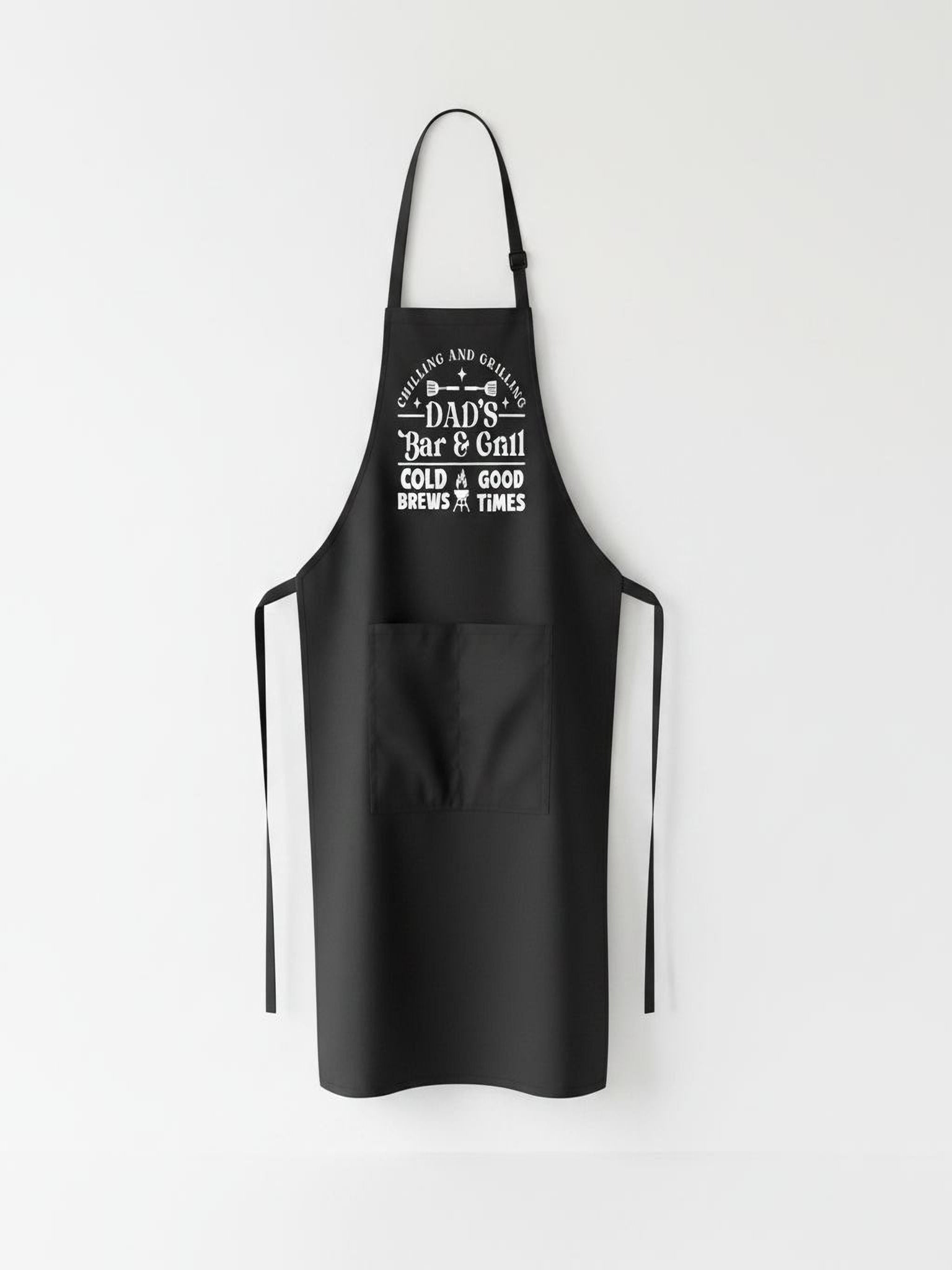 Dad’s Bar and Grill apron featuring funny BBQ typography design worn by man grilling outdoors in backyard.