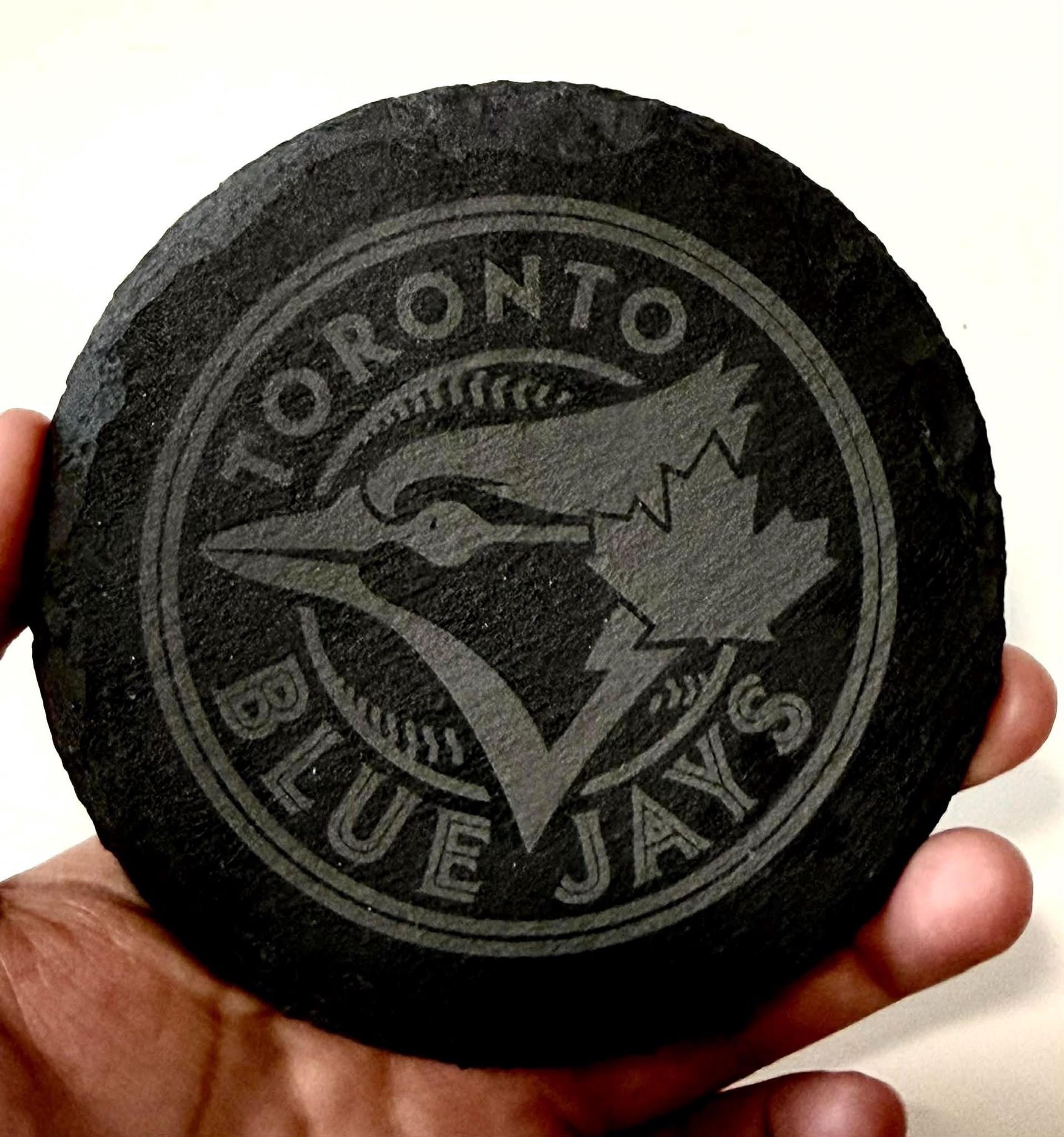 A hand holding a black coaster with the logo of the Toronto Blue Jays baseball team printed on it.