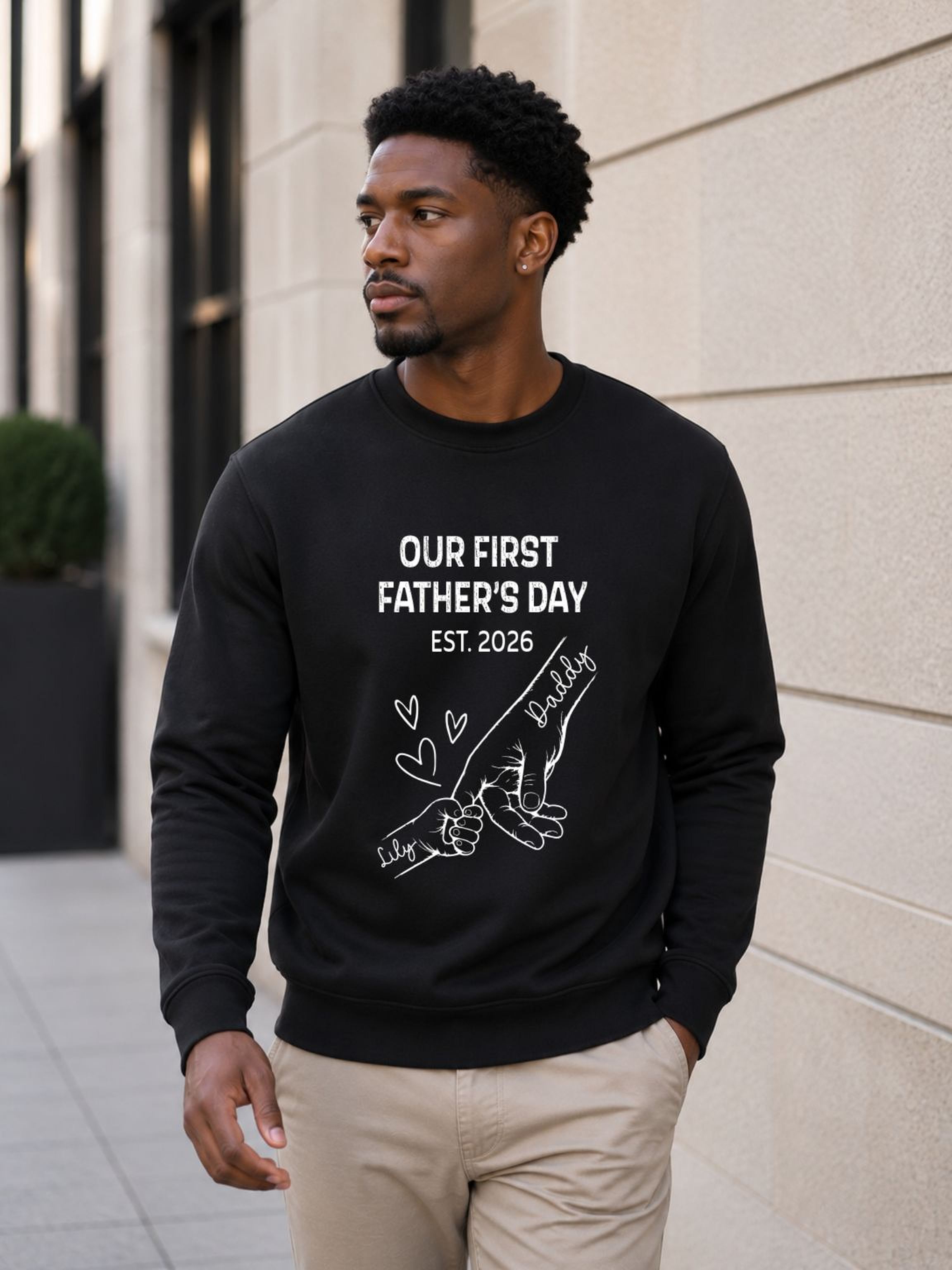 sweatshirt featuring personalized Our First Father’s Day design with minimalist daddy and baby hand outline artwork worn by male model outdoors.