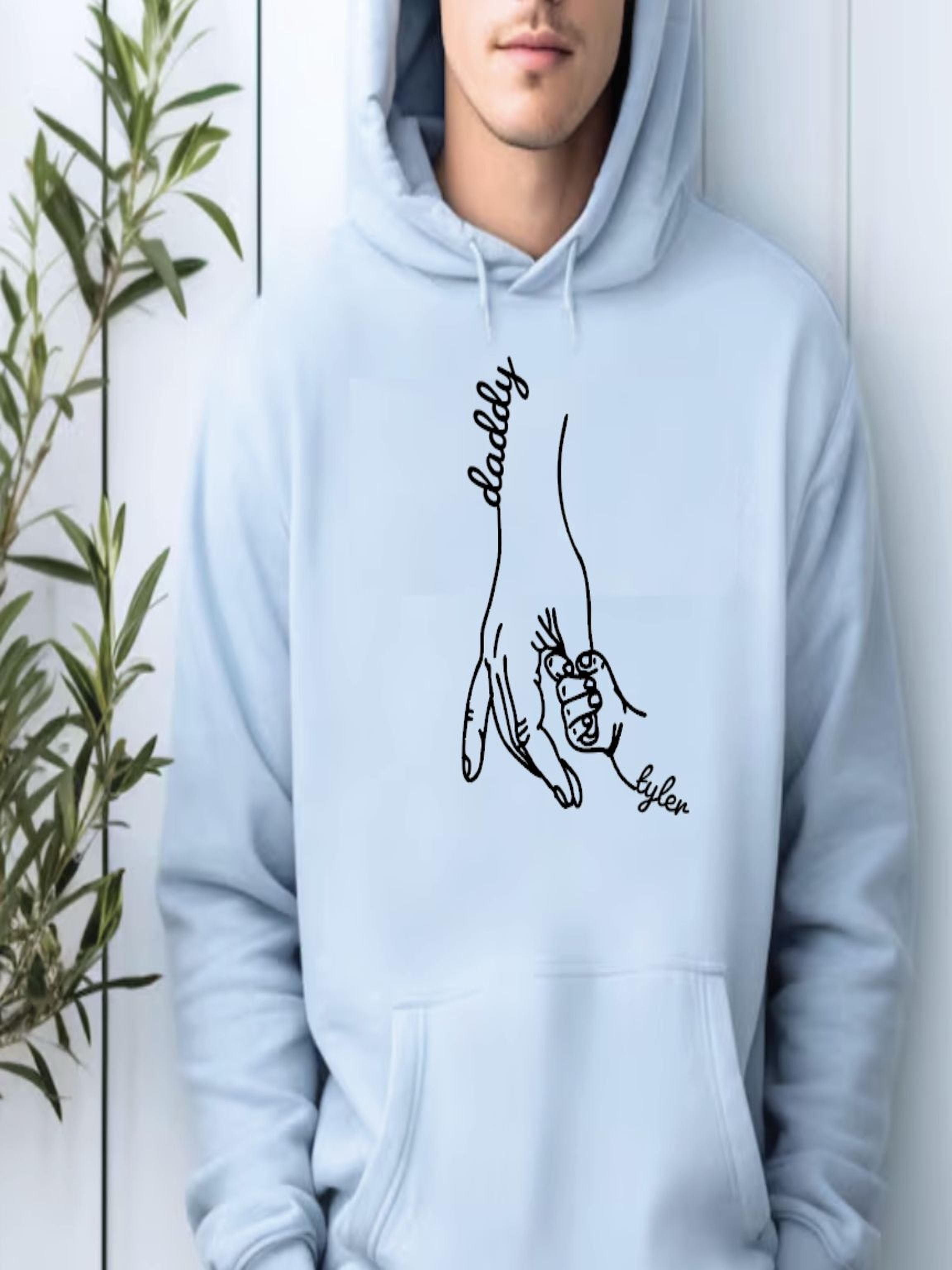 A person wearing a light blue hoodie with a graphic design depicting a hand holding a child's hand.