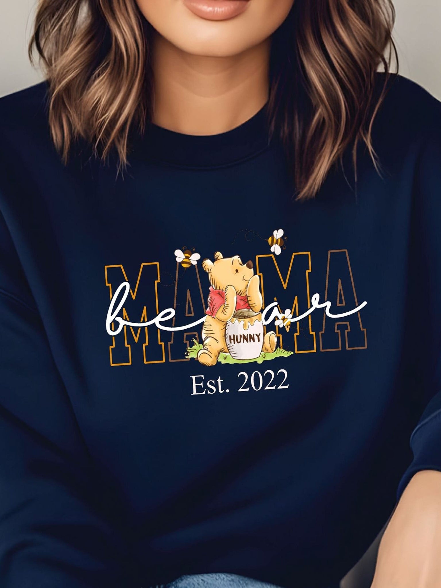 A woman wearing a navy blue sweatshirt with a Winnie the Pooh-themed design and text.