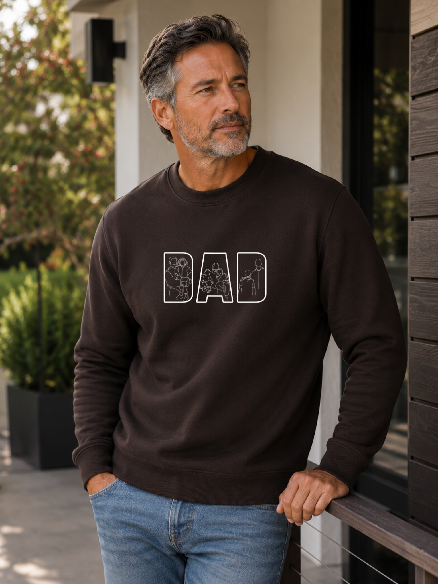 Minimalist brown dad sweatshirt with white outline family artwork inside DAD lettering worn by male model outdoors.