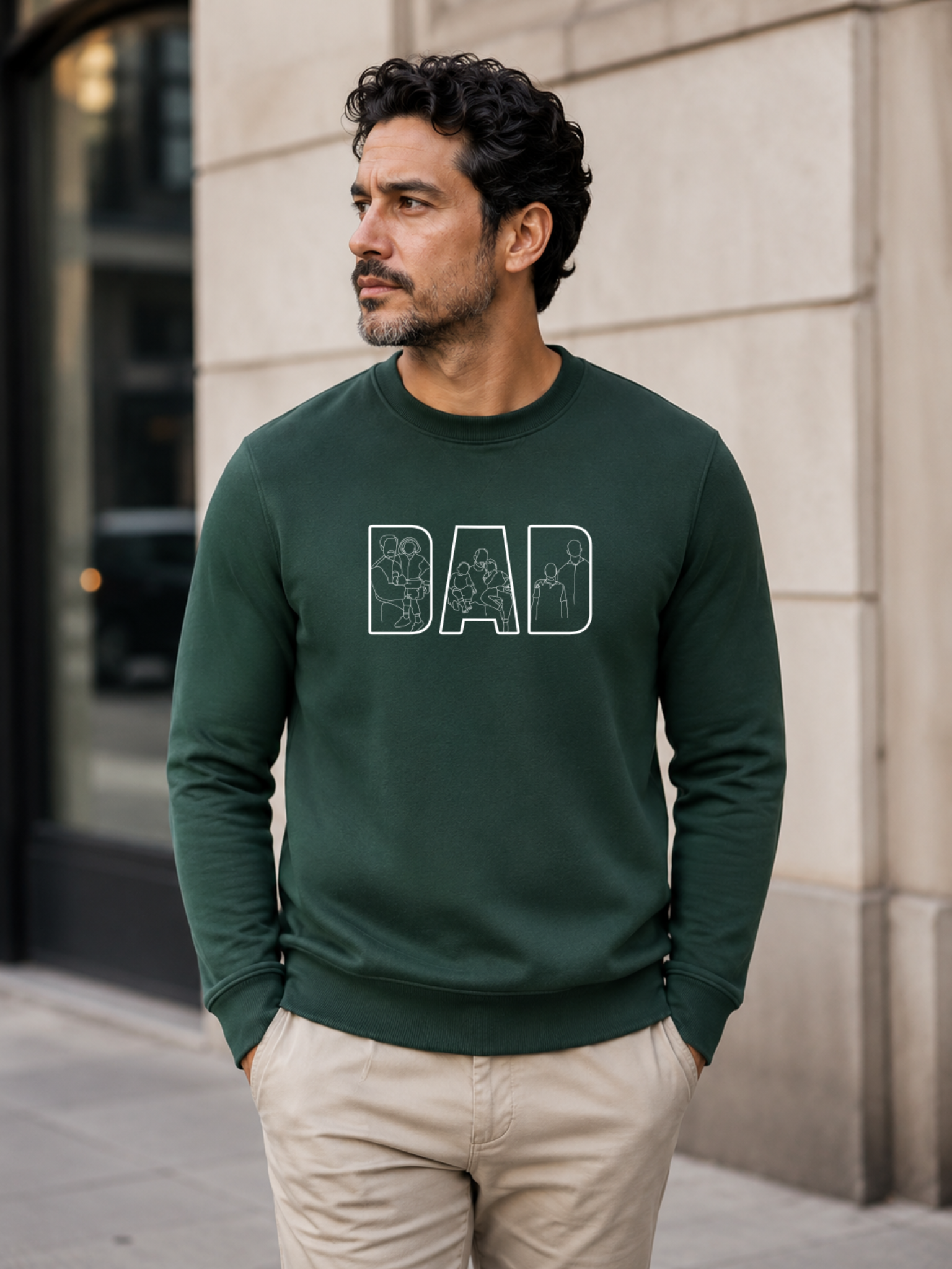 Minimalist green dad sweatshirt with white outline family artwork inside DAD lettering worn by male model outdoors.