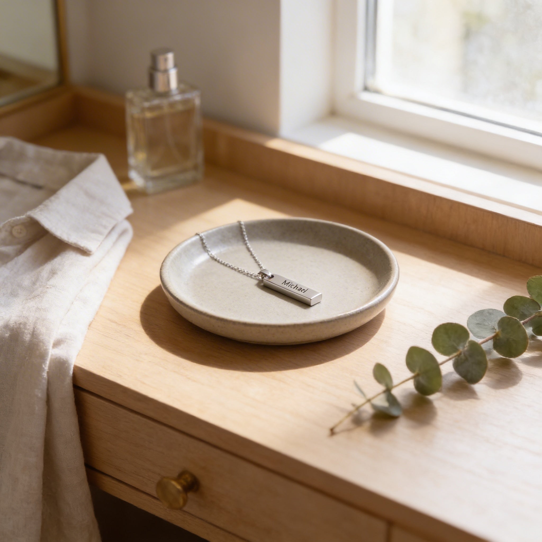 a wooden dresser with a round plate holding a necklace and a small bottle of perfume. There is also a plant and a towel on the dresser.
