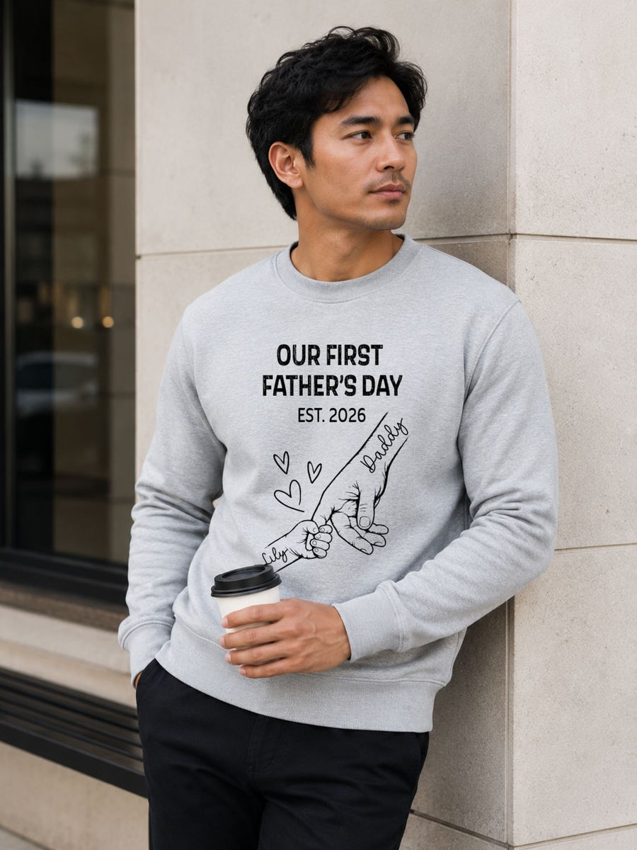 sweatshirt featuring personalized Our First Father’s Day design with minimalist daddy and baby hand outline artwork worn by male model outdoors.
