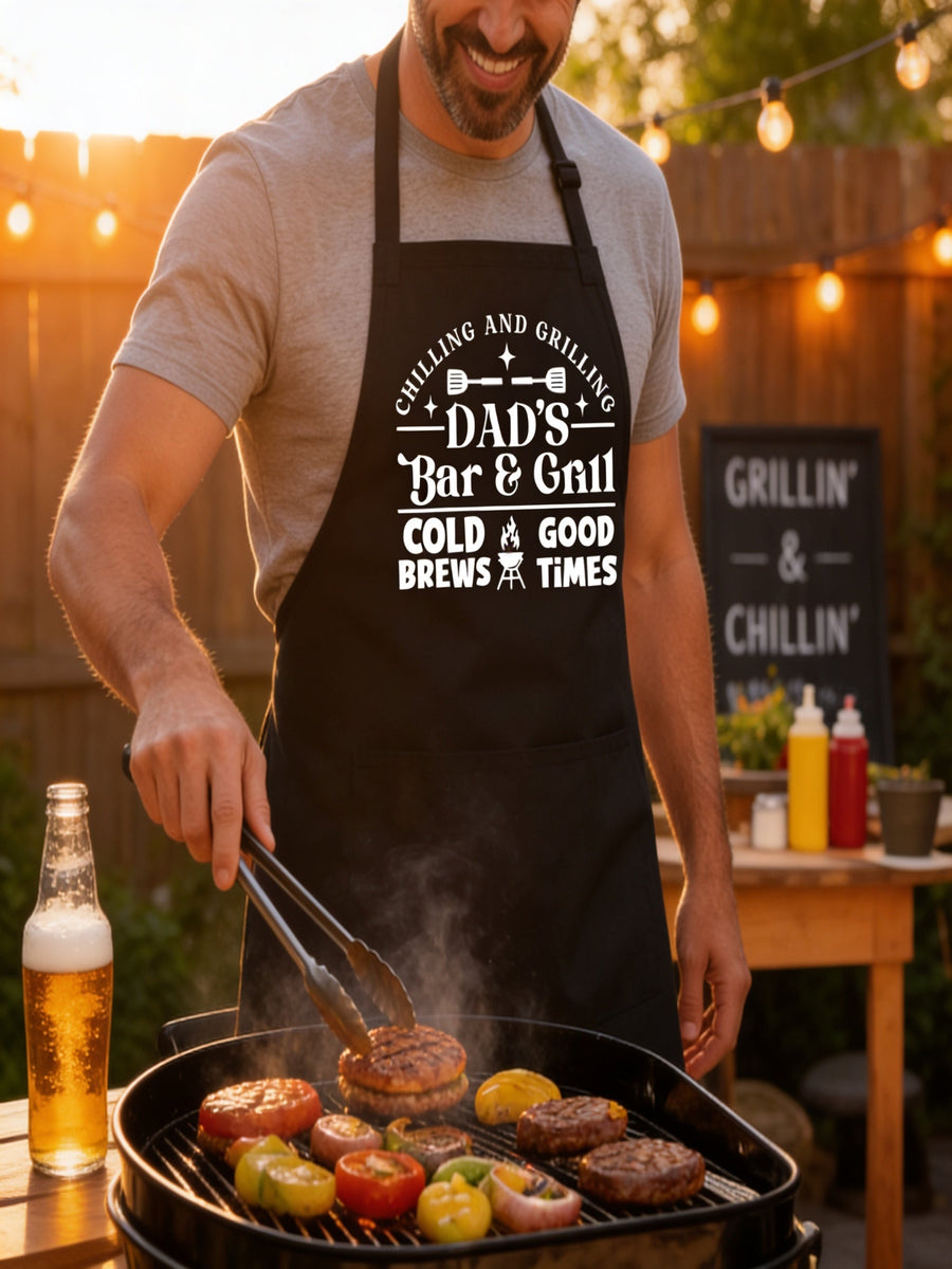 Dad’s Bar and Grill apron featuring funny BBQ typography design worn by man grilling outdoors in backyard.
