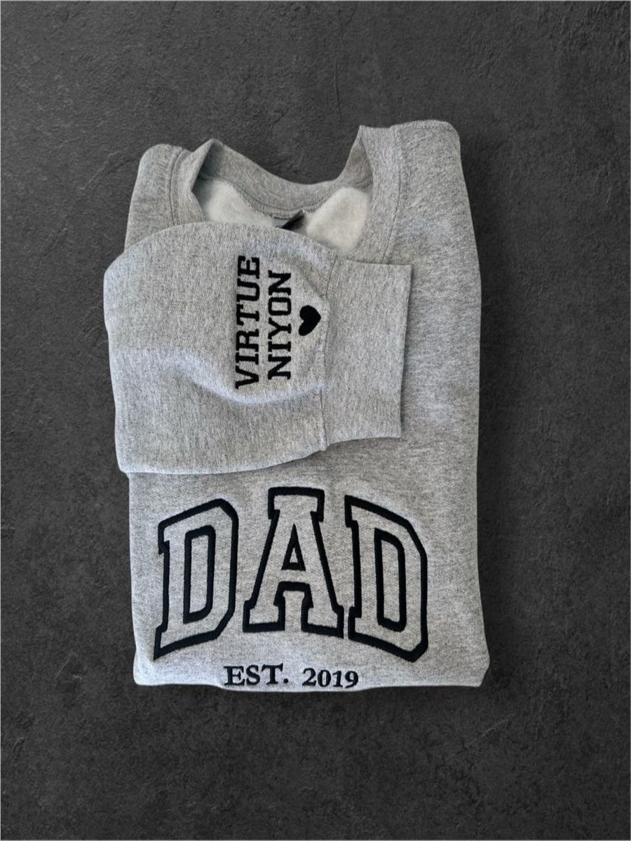 A gray sweatshirt with the text "VIRUTE N'YON" and "DAD" printed on it, along with the year "EST. 2019" below.