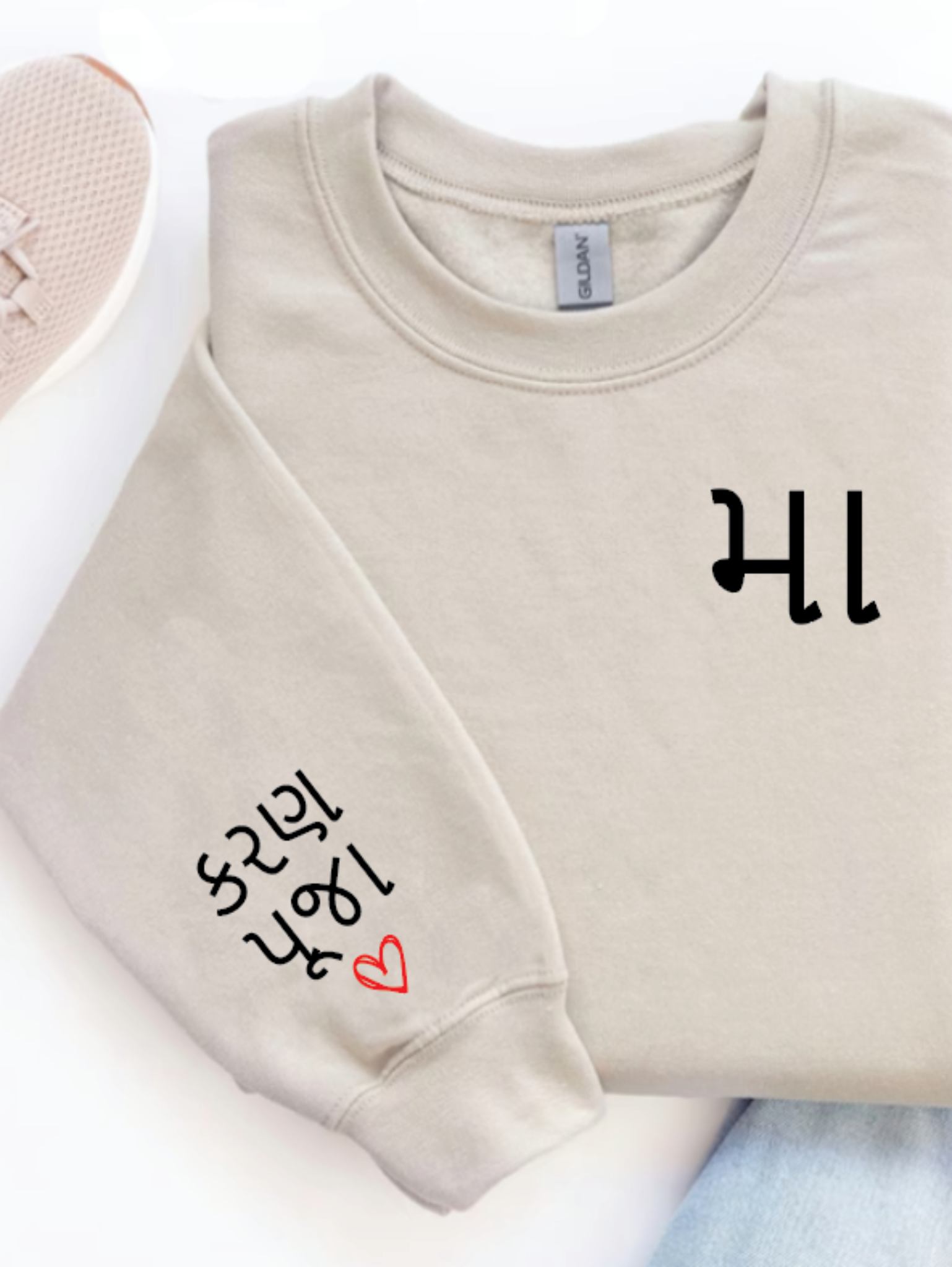 Folded beige sweatshirt with 'HI' and 'hello' text, pink sneakers, and jeans on a white background