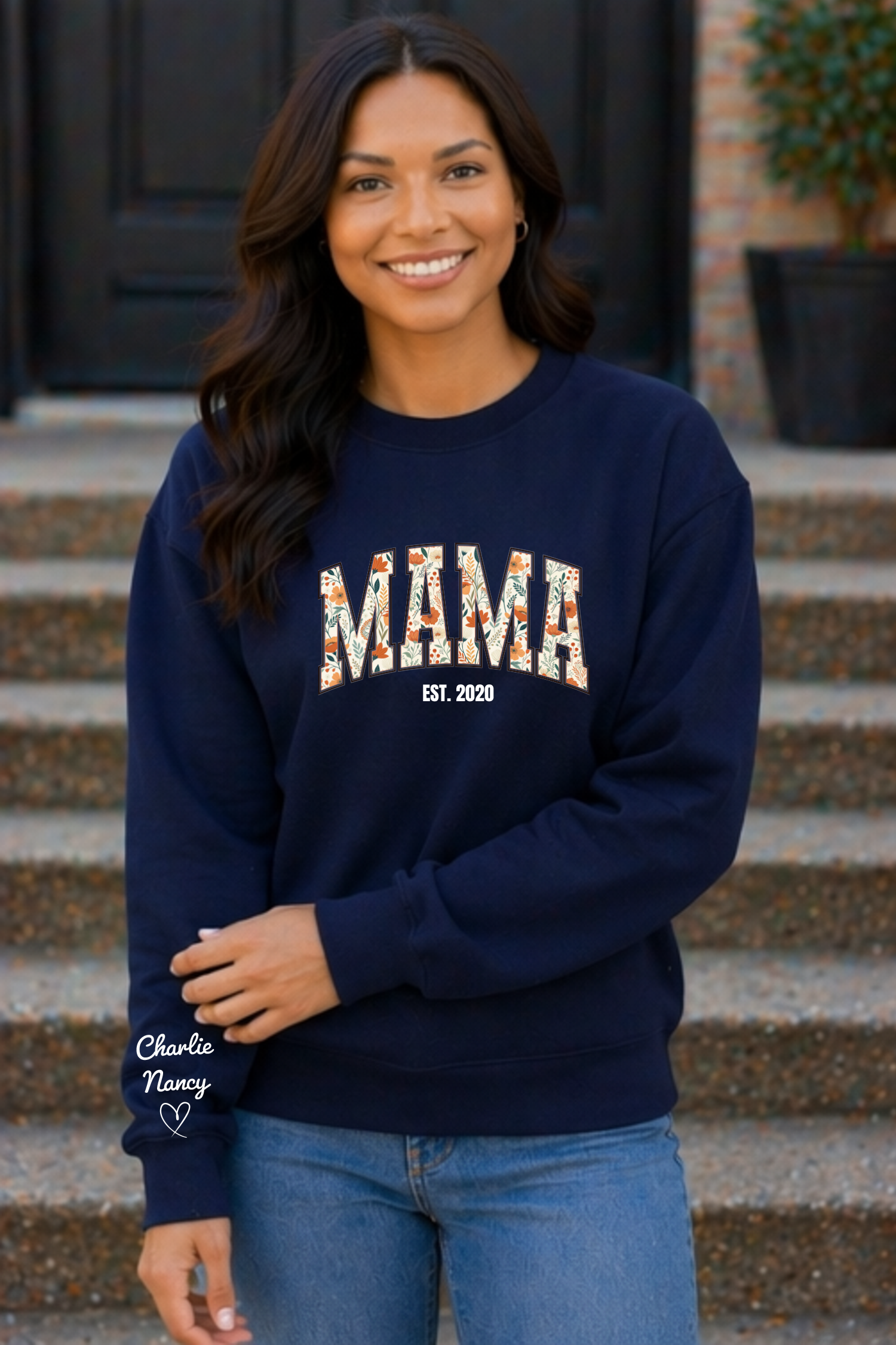 Woman wearing a navy sweatshirt with 'MAMA EST. 2020' text, standing on steps.