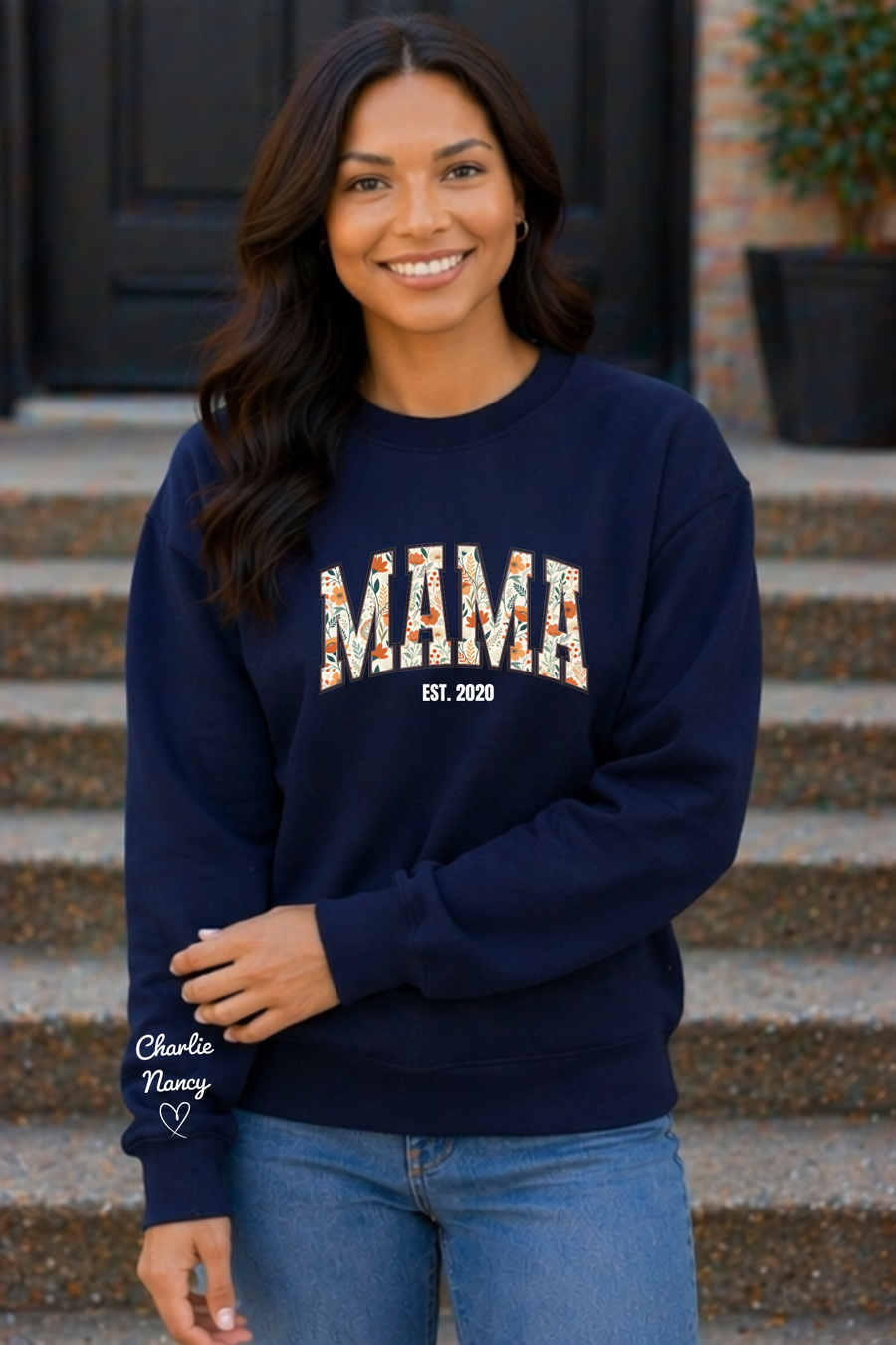 Woman wearing a navy sweatshirt with 'MAMA EST. 2020' text, standing on steps.