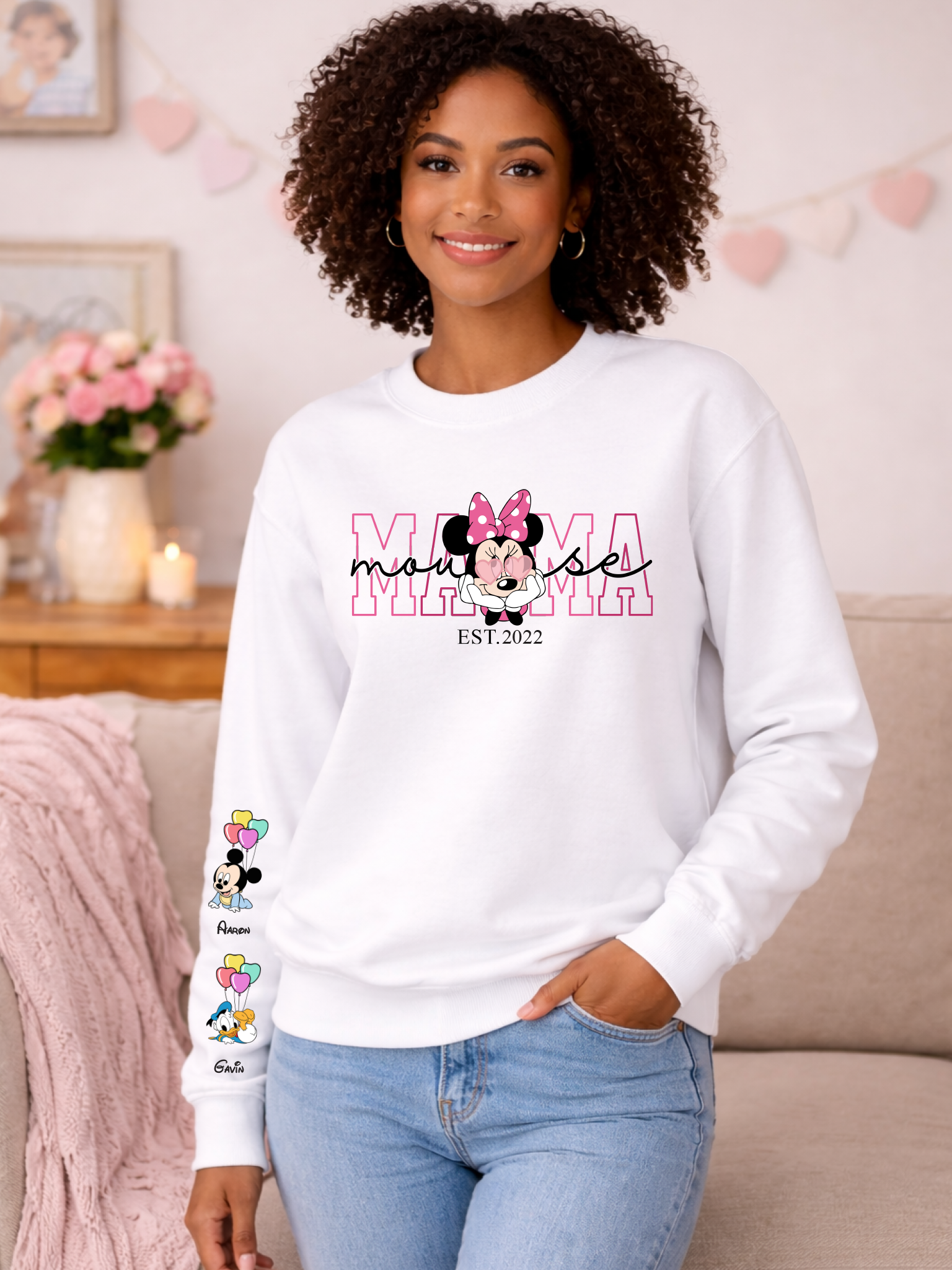 Woman wearing a white sweatshirt with 'Minnie Mouse' design and text, standing in a cozy living room.