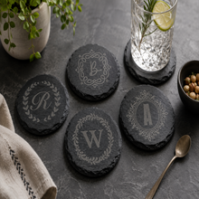 Personalized round black slate coaster engraved with custom monogram initial, elegant decorative border design, custom wedding and housewarming gift.