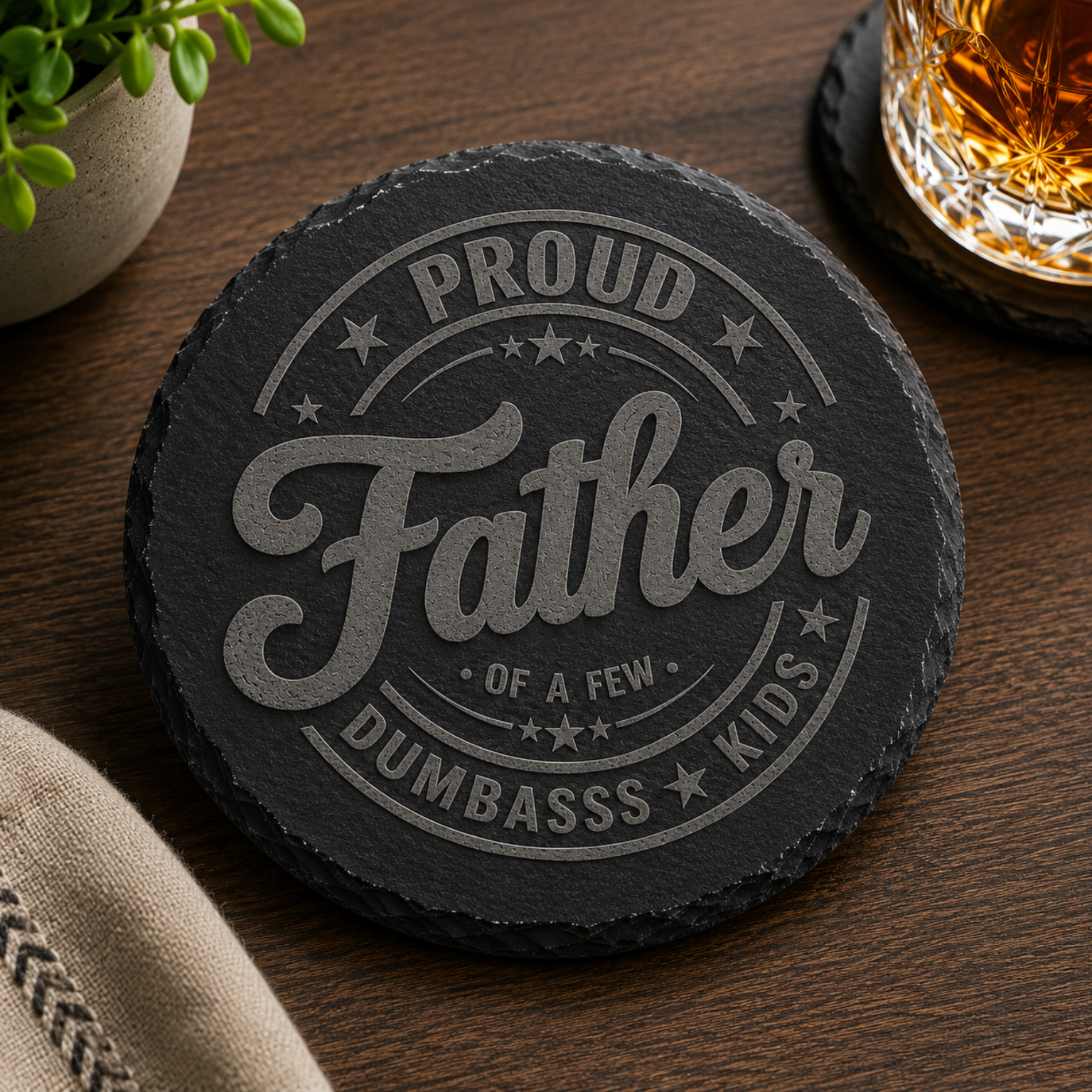 Funny engraved round black slate coaster featuring the phrase "Proud Father of a Few Dumbass Kids", unique Father's Day gift for dads with a sense of humor.