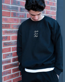 Person wearing a black sweatshirt with white text against a brick wall