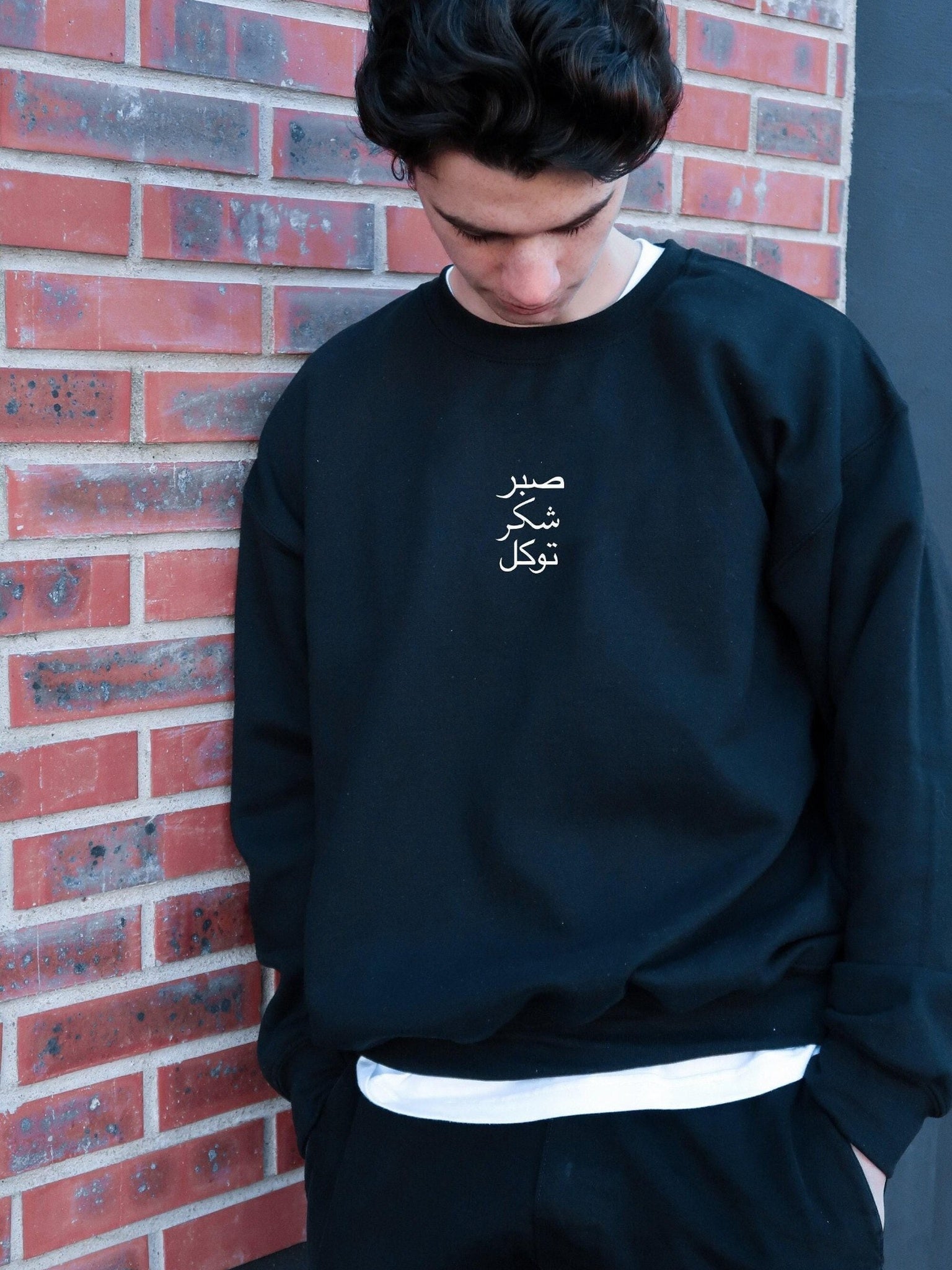 Person wearing a black sweatshirt with white text against a brick wall